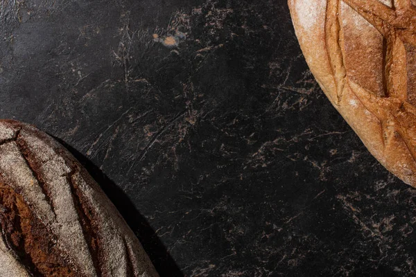 Vista superior de pão branco e marrom cozido no forno fresco na superfície preta de pedra — Fotografia de Stock