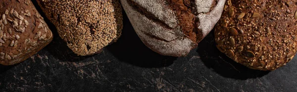 Vista superior de pão de grão inteiro cozido no forno fresco na superfície preta de pedra, tiro panorâmico — Fotografia de Stock
