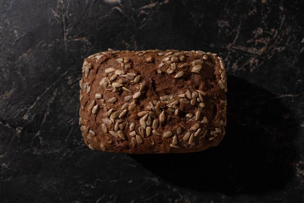 Top view of fresh baked brown bread loaf with sunflower seeds on stone black surface — Stock Photo