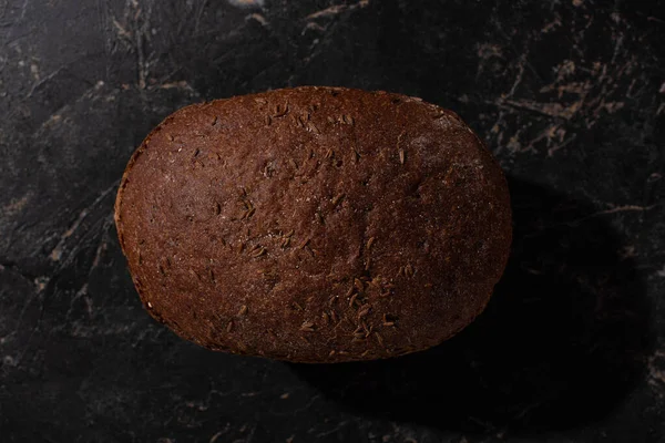 Vista dall'alto della pagnotta di pane marrone appena sfornato sulla superficie nera di pietra — Foto stock