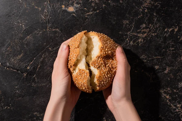 Cropped view of woman holding torn sesame bun on stone black surface — Stock Photo