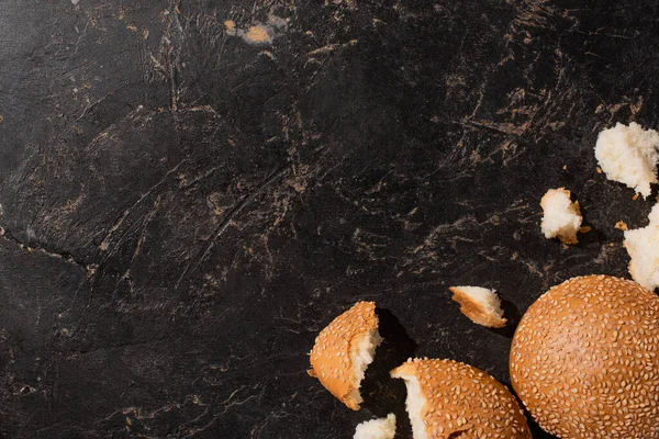 Top view of torn sesame buns on stone black surface — Stock Photo