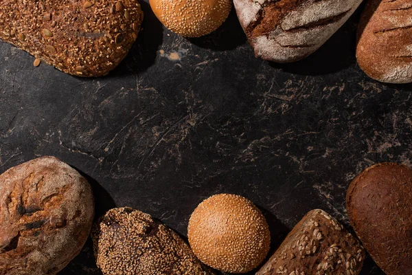 Vue de dessus du pain frais cuit au four et des petits pains sur la surface noire de pierre — Photo de stock