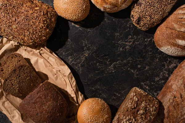 Vue de dessus du pain frais coupé et entier sur la surface noire de pierre — Photo de stock
