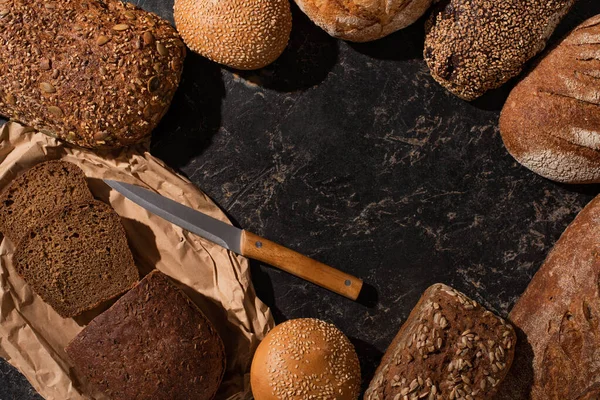 Vista superior de corte fresco y pan entero con cuchillo en la superficie de piedra negro — Stock Photo