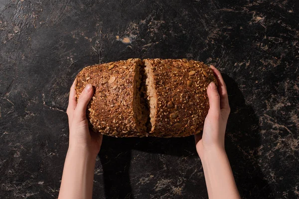 Vista ritagliata della donna che tiene il pane integrale tagliato su pietra superficie nera — Foto stock