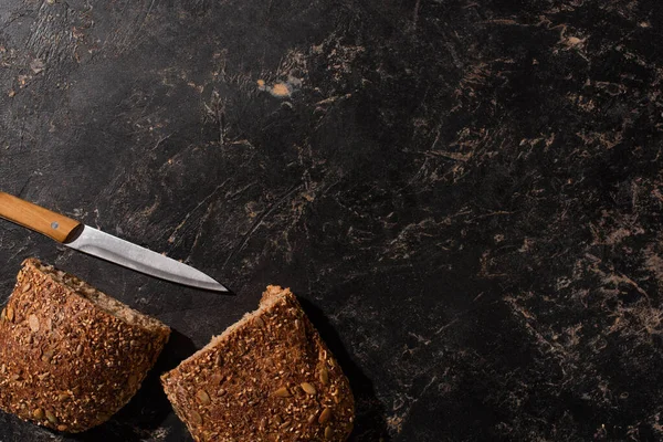 Вид зверху на розрізаний цільний зерновий хліб з ножем на чорній поверхні каменю — стокове фото