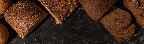 Top view of cut whole grain bread on stone black surface, panoramic shot — Stock Photo