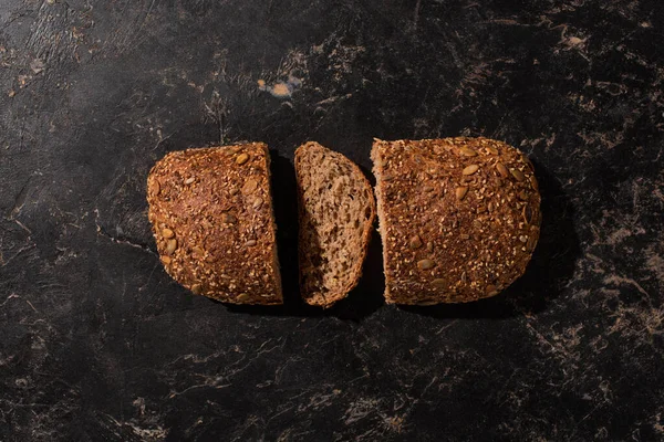 Top view of cut whole grain bread on stone black surface — Stock Photo