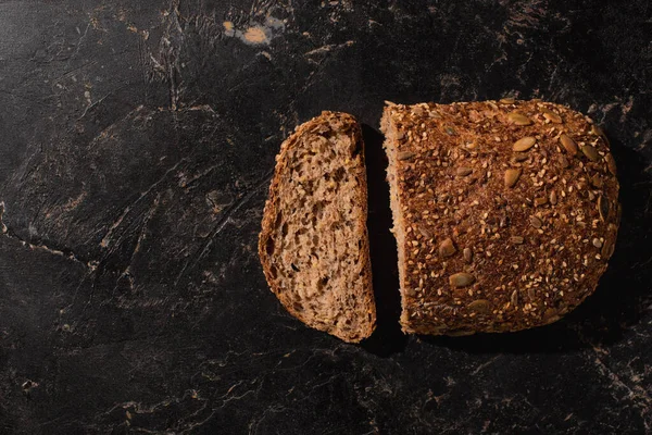 Vue du dessus du pain coupé à grains entiers sur la surface noire de pierre — Photo de stock