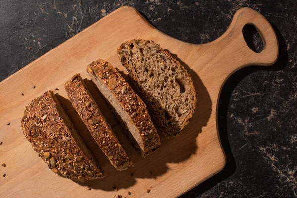 Ansicht von geschnittenem Vollkornbrot auf Schneidebrett auf steinschwarzer Oberfläche — Stockfoto