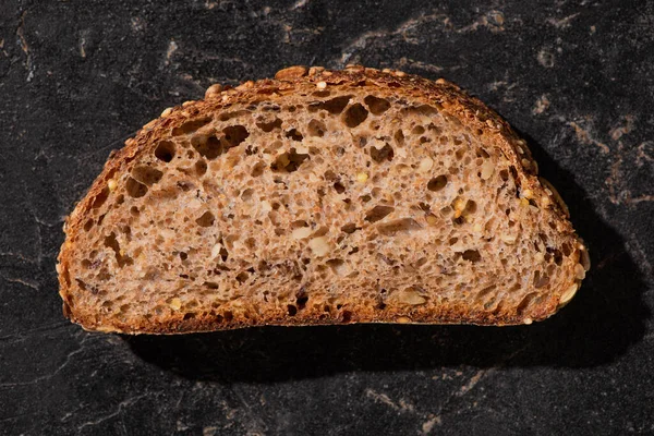 Vista superior de la rebanada de pan de grano entero recién horneado en la superficie de piedra negro - foto de stock