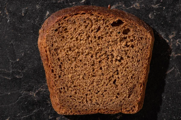 Vista dall'alto della fetta di pane marrone appena sfornato sulla superficie di pietra nera — Foto stock