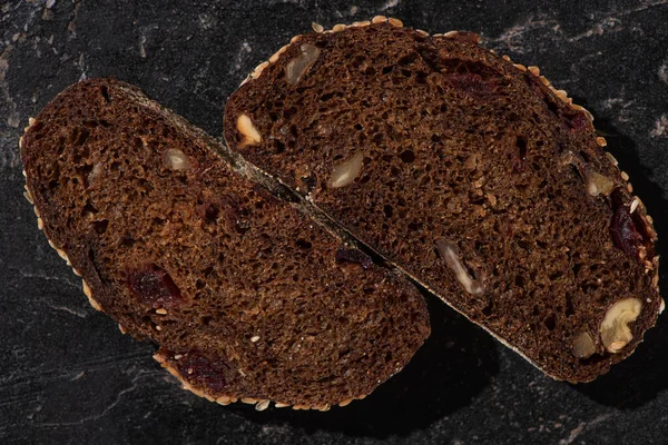 Draufsicht auf frisch gebackene Schwarzbrotscheiben mit Nüssen auf steinschwarzer Oberfläche — Stockfoto