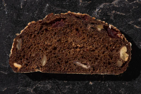 Vista dall'alto della fetta di pane nero appena sfornato con noci sulla superficie nera di pietra — Foto stock