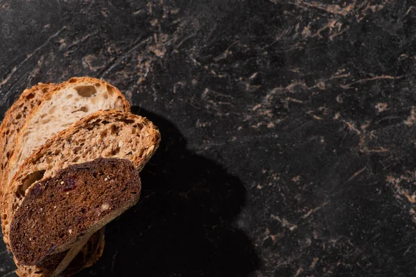 Draufsicht auf frisch gebackene Brotscheiben auf steinschwarzer Oberfläche — Stockfoto