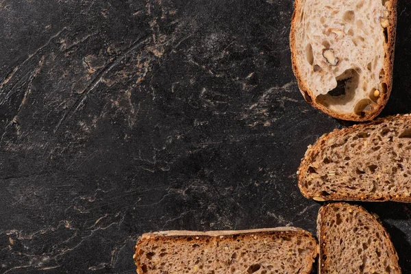 Draufsicht auf frisch gebackene Brotscheiben auf steinschwarzer Oberfläche — Stockfoto