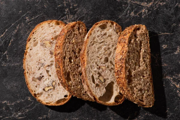 Draufsicht auf frisch gebackene Brotscheiben auf steinschwarzer Oberfläche — Stockfoto