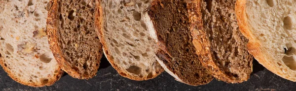 Vista superior de fatias de pão cozido no forno fresco na superfície preta de pedra, tiro panorâmico — Fotografia de Stock