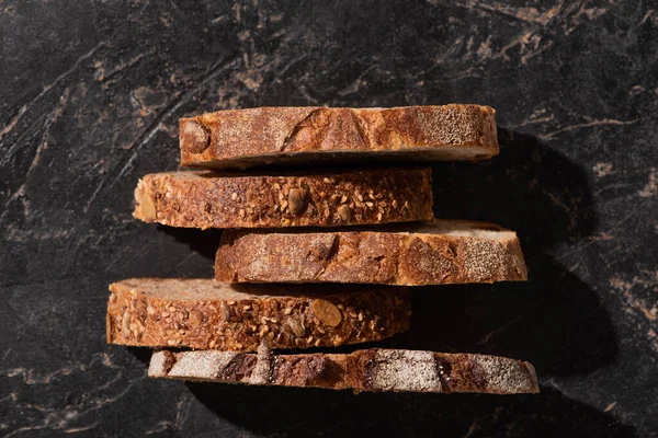 Draufsicht auf frische Brotscheiben auf steinschwarzer Oberfläche — Stockfoto