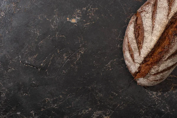 Top view of organic brown bread loaf on stone black surface — Stock Photo