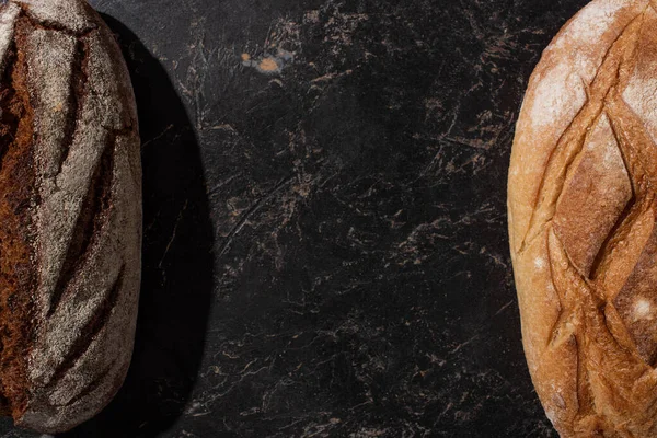 Draufsicht auf frisch gebackenes braunes und weißes Brot auf schwarzer Steinoberfläche — Stockfoto