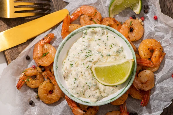 Top view of fried shrimps on parchment paper with sauce and lime near cutlery — Stock Photo