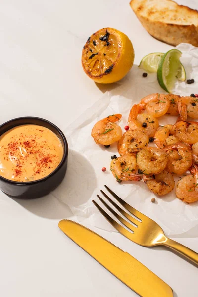 Fried shrimps on parchment paper with sauce and lime near golden cutlery on white background — Stock Photo