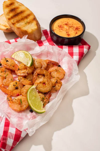 Crevettes frites sur papier parchemin avec sauce, pain grillé et citron vert sur fond blanc avec serviette à carreaux rouge — Photo de stock