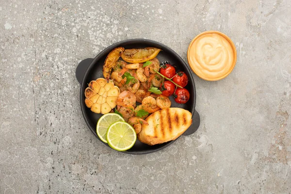 Top view of fried shrimps with grilled toasts, vegetables and lime near sauce on grey concrete background — Stock Photo