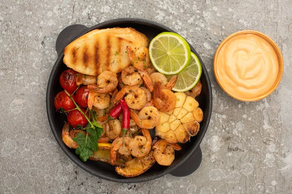 Draufsicht auf gebratene Garnelen mit gegrillten Toasts, Gemüse und Limette mit Sauce auf grauem Betonhintergrund — Stockfoto