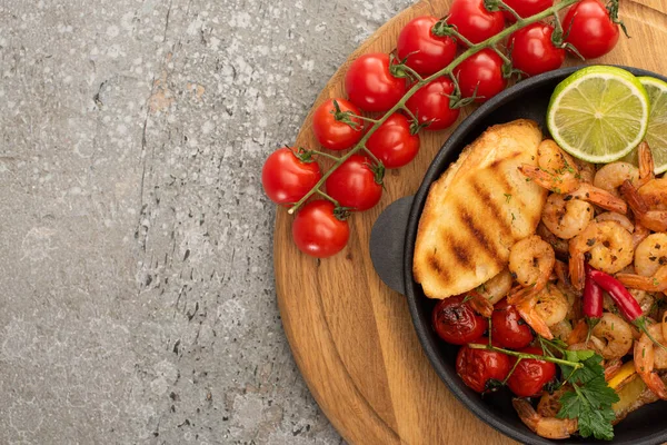 Vue de dessus des crevettes frites avec des toasts grillés, légumes, tomates cerises et citron vert sur panneau de bois sur fond de béton gris — Photo de stock