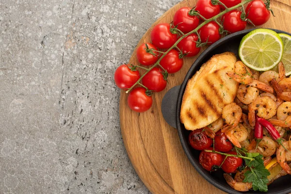 Vista superior de camarões fritos com torradas grelhadas, legumes, tomates cereja e limão em tábua de madeira sobre fundo de concreto cinza — Fotografia de Stock