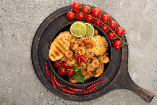 Top view of fried shrimps with grilled toasts, vegetables, cherry tomatoes and lime on wooden board on grey concrete background — Stock Photo