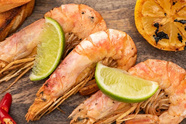 Close up view of fried shrimps with lemon, chili and lime on wooden board — Stock Photo