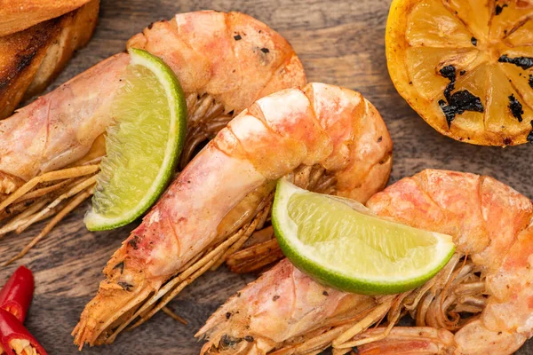 Vista de cerca de camarones fritos con limón, chile y lima sobre tabla de madera - foto de stock