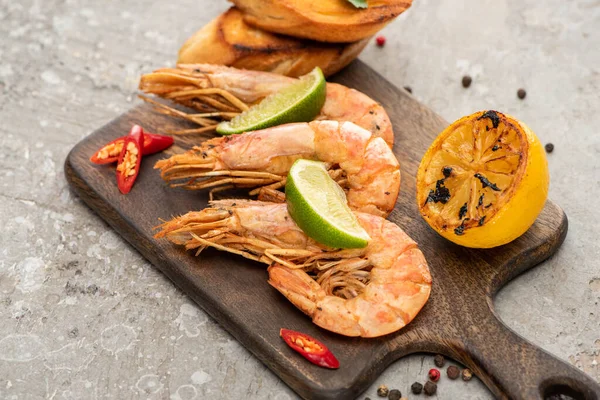 Gamberetti fritti con pane tostato alla griglia, limone e lime su tavola di legno su fondo grigio cemento — Foto stock