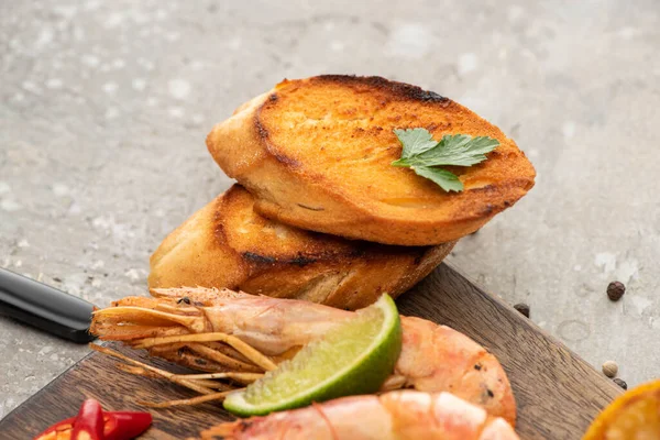 Close up view of fried shrimps with grilled toasts and lime on wooden board on grey concrete background — Stock Photo