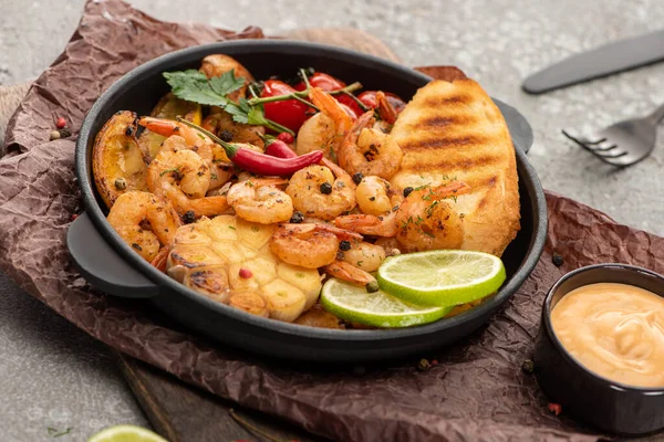Selective focus of fried shrimps with grilled toasts, vegetables and lime on grey concrete background with cutlery — Stock Photo