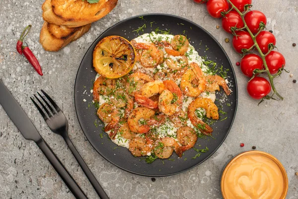 Vista superior de camarões fritos em molho com endro e limão perto de talheres, tomates cereja e torradas em fundo de concreto cinza — Fotografia de Stock