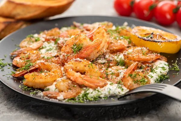 Selective focus of fried shrimps in sauce with dill and lemon in black plate on grey concrete background — Stock Photo