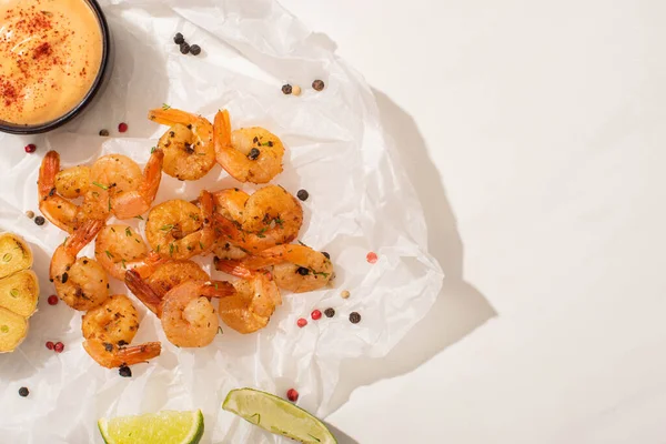Vue du dessus des crevettes frites sur papier parchemin avec poivre, sauce et citron vert sur fond blanc — Photo de stock