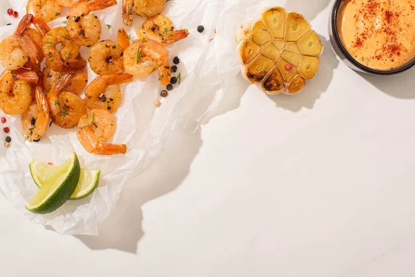 Vue du dessus des crevettes frites sur papier parchemin avec maïs grillé, poivre, sauce et citron vert sur fond blanc — Photo de stock