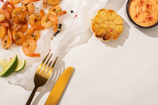 Draufsicht auf gebratene Garnelen auf Pergamentpapier mit Besteck, gegrilltem Mais, Pfeffer, Sauce und Limette auf weißem Hintergrund — Stockfoto