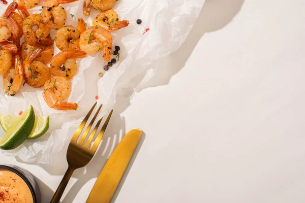 Vista dall'alto di gamberetti fritti su carta pergamena con posate, pepe, salsa e lime su sfondo bianco — Foto stock