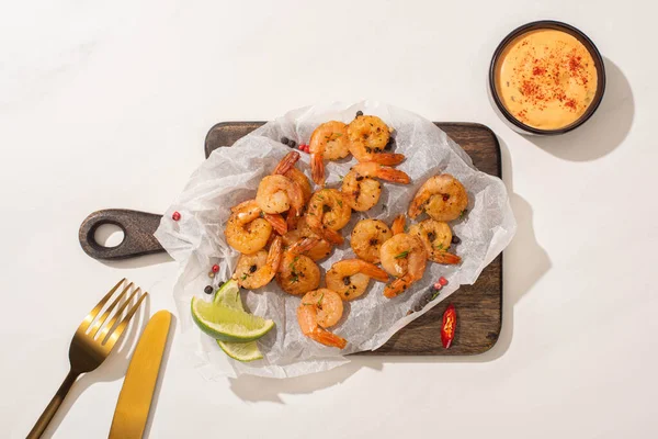 Vista dall'alto di gamberetti fritti su carta pergamena su tavola di legno con posate, peperoncino, salsa e lime su fondo bianco — Foto stock