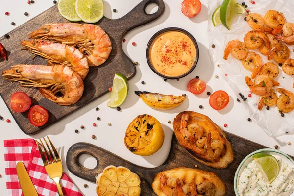 Top view of fried shrimps on parchment paper and boards with cutlery, vegetables, sauce and lime on white background — Stock Photo