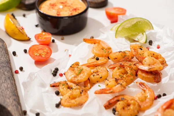 Enfoque selectivo de camarones fritos con salsa, lima y pimienta en papel pergamino blanco - foto de stock