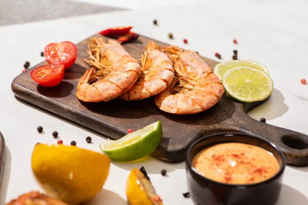 Selektiver Fokus gebratener Garnelen auf Holzbrett in der Nähe von Zitrone, Sauce und Limette auf weißem Hintergrund — Stockfoto