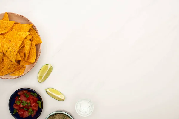 Top view of tequila with lime, chili pepper and nachos in plate on white marble surface — Stock Photo